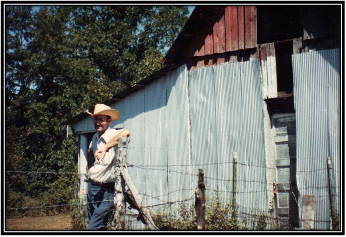 Cathy's dad leaning on a fence post in front of a barn