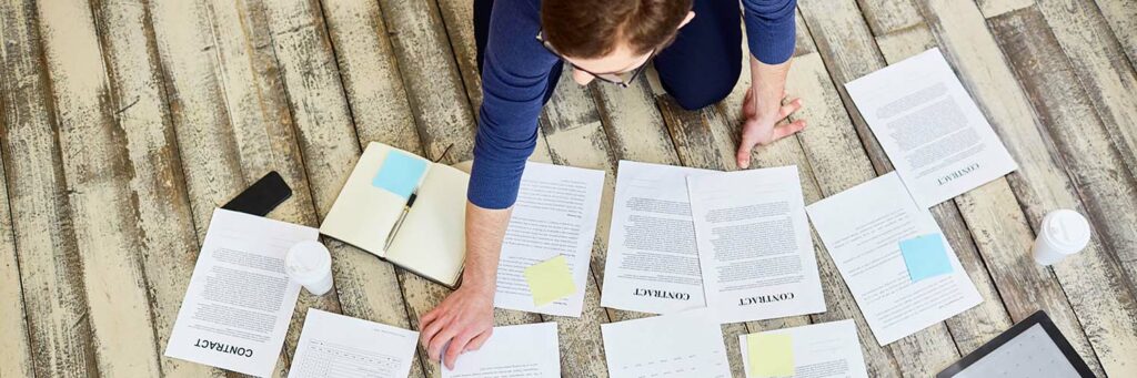 Above view of unrecognizable businessman laying out documents on wooden floor in office