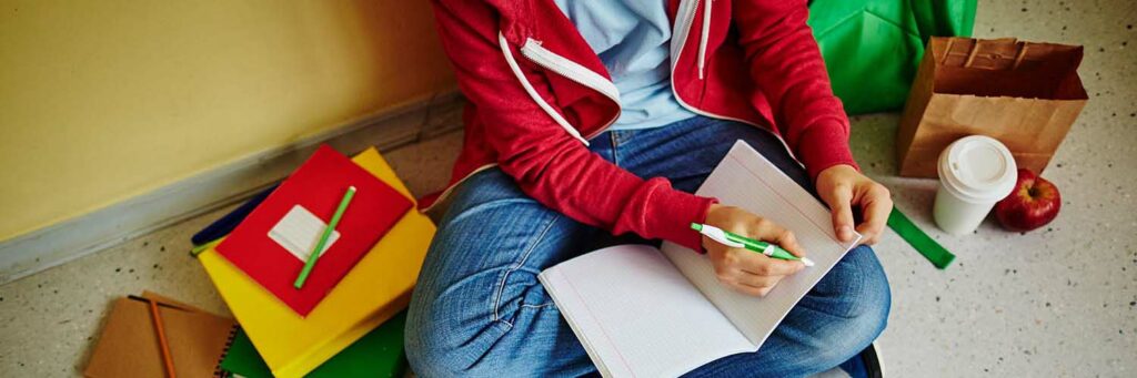 Schoolboy making notes in exercise-book while sitting on the floor