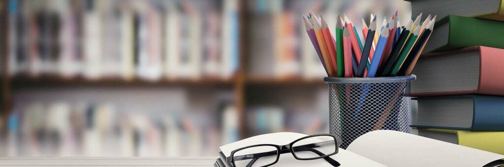 School supplies on desk against library shelf