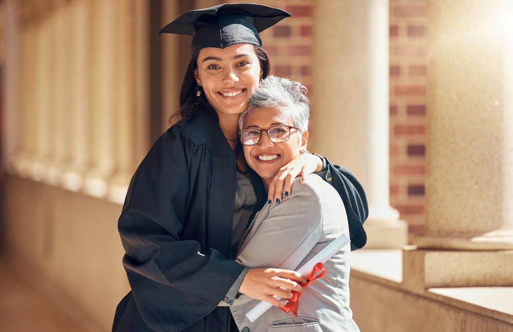 Daughter in graduation cap and gown hugging mom