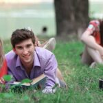 several pairs of students with books lying on the grass in the Park.