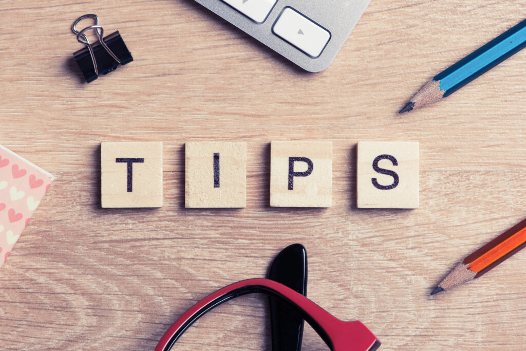 Corner of laptop with pencils, binder clip, glasses, and tiles that spell "TIPS" on desk.