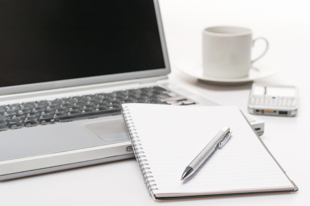 Laptop with notebook, pen, coffee cup, and phone