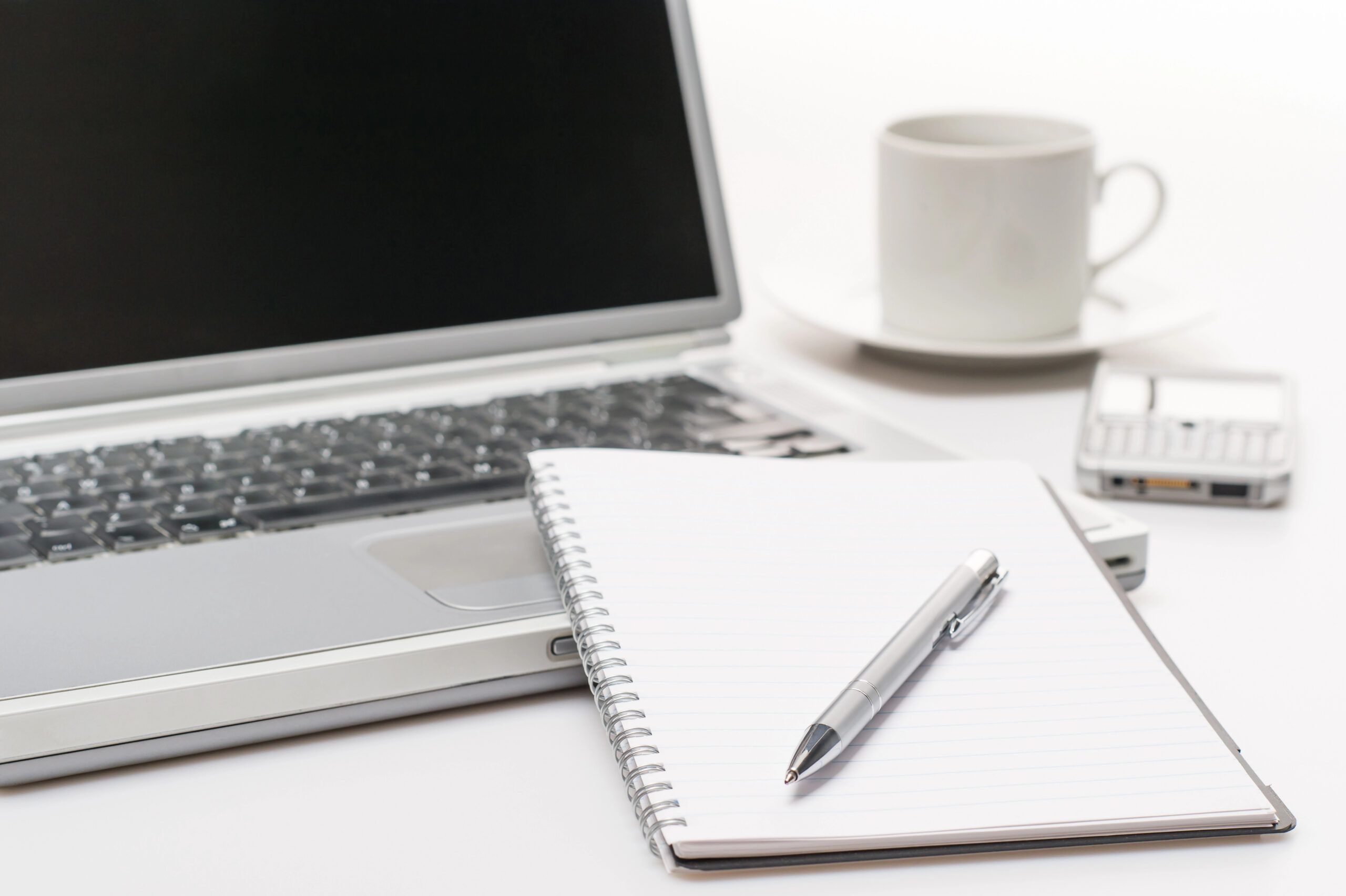 Laptop with notebook, pen, coffee cup, and phone
